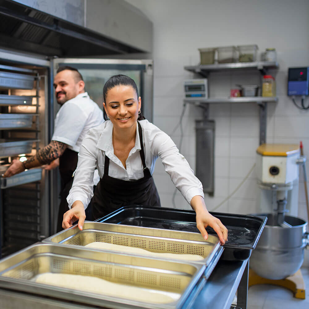 kitchen staff organizing empura accessories including stainless steel food pans and trays in prep area